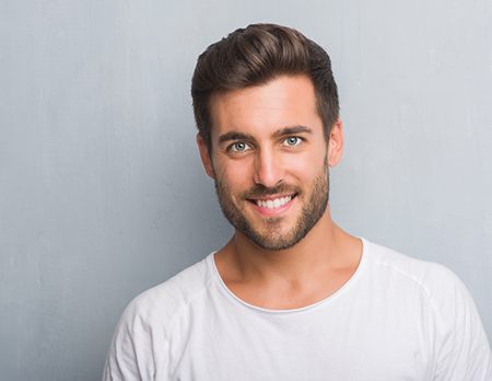 A photo of a handsome young man over grey background benefiting from facial implants